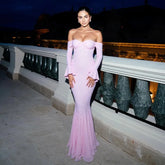 Woman in a pink off-shoulder gown standing on a balcony at night.