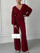 Woman wearing a burgundy outfit with a white handbag against a gray wall.