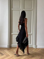 Woman in a black dress standing in a room with wooden flooring and white walls.