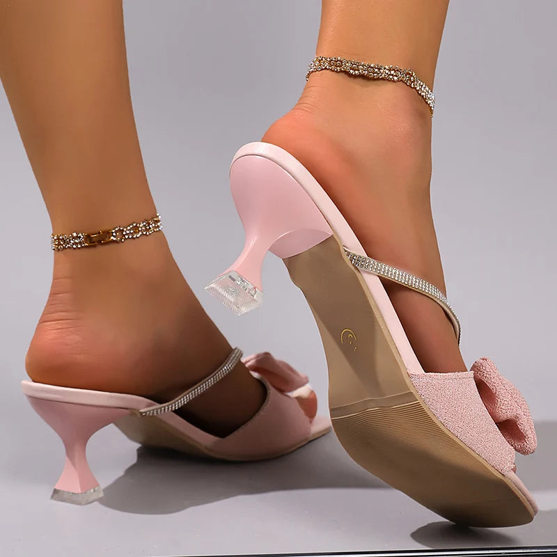 Pink high-heeled shoes with decorative straps on a neutral background