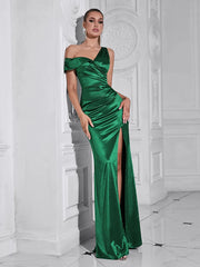 Woman wearing a green satin one-shoulder dress with a high slit in a white room.
