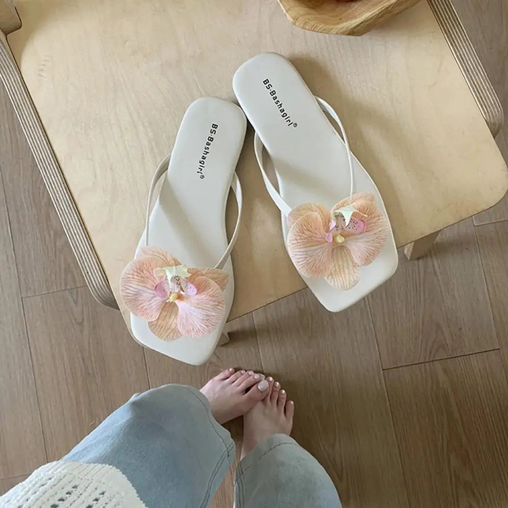 White flip-flops with pink floral designs on a wooden floor.