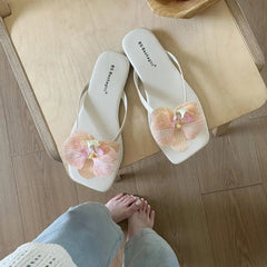 White flip-flops with pink floral designs on a wooden floor.