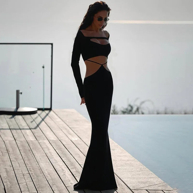 Woman in a black evening gown standing on a wooden deck by a pool.
