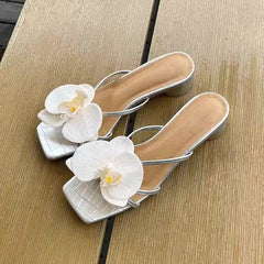 Silver high-heeled sandals with white floral decorations on a wooden surface