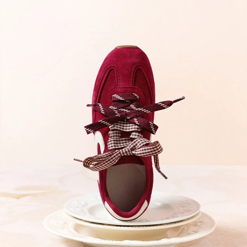 Close-up of a single red suede sneaker showing the lace-up detail and bow.