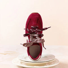 Close-up of a single red suede sneaker showing the lace-up detail and bow.