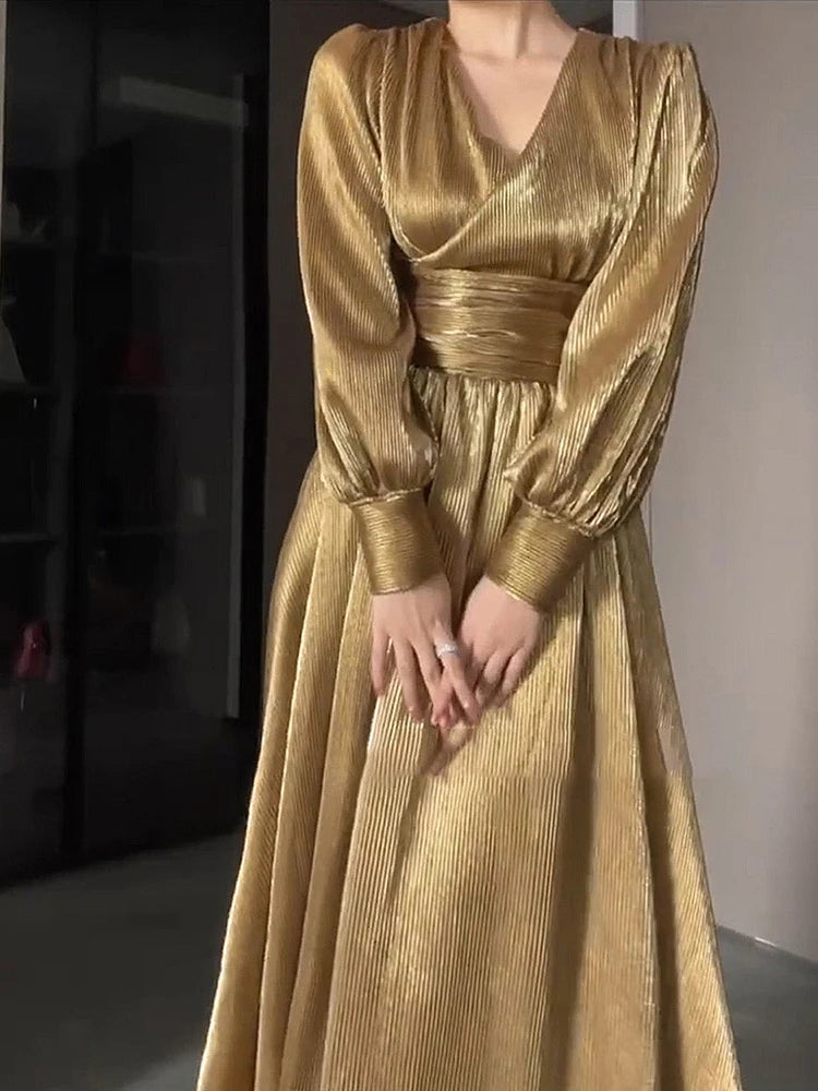 Gold dress with long sleeves and a fitted waist on a neutral background