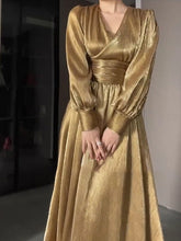 Gold dress with long sleeves and a fitted waist on a neutral background