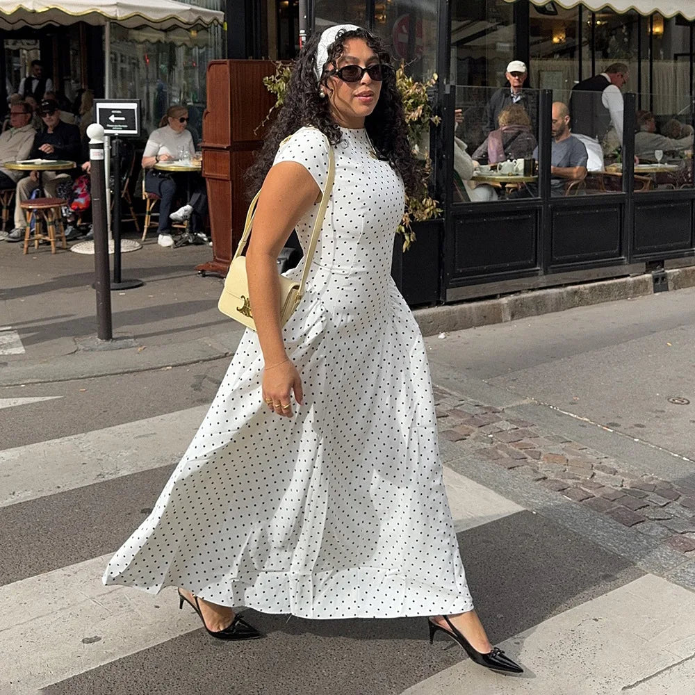 Woman in a white polka dot dress walking on a city street.