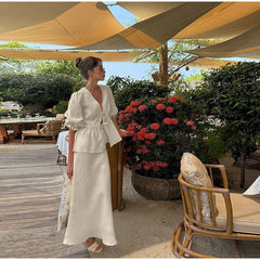 Woman in a white dress standing under a canopy with floral decorations and outdoor furniture.
