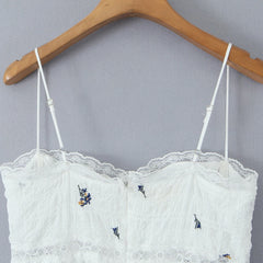 White lace top with embroidered details on a wooden hanger against a gray background