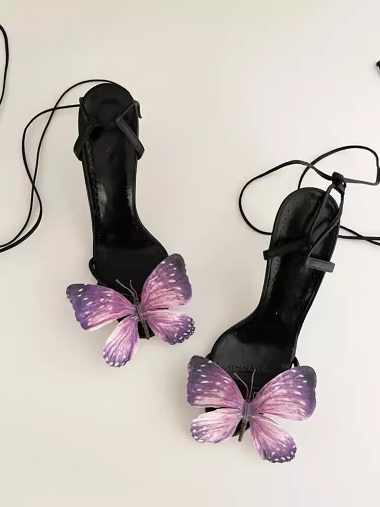 Black high-heeled shoes with purple butterfly decorations on a white background