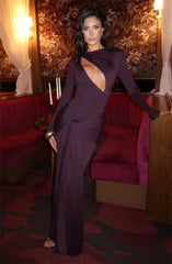 Woman in a long, dark purple dress sitting on a red couch in an elegant room.