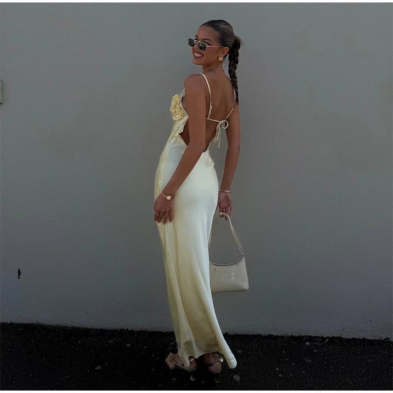 Woman in a long white dress holding a handbag against a plain wall.