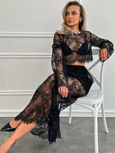 Woman wearing a black lace outfit sitting on a white chair against a gray wall.