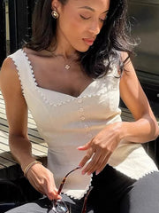Woman wearing a white sleeveless top with lace details, sitting outdoors.
