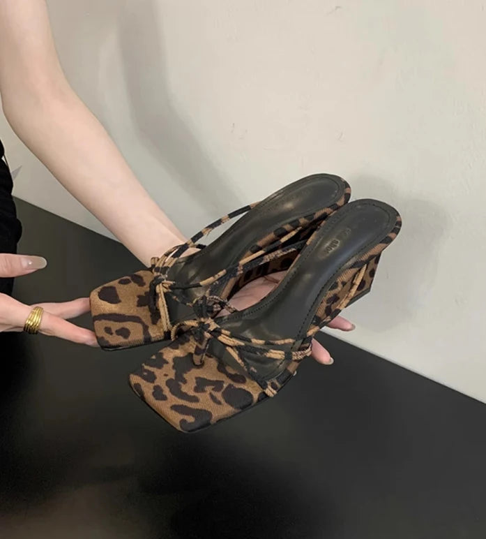 Leopard print high-heeled shoes held by a person against a neutral background