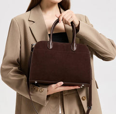 Person holding a brown leather handbag against a neutral background
