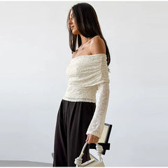 Woman wearing a white off-shoulder top and black pants against a plain background