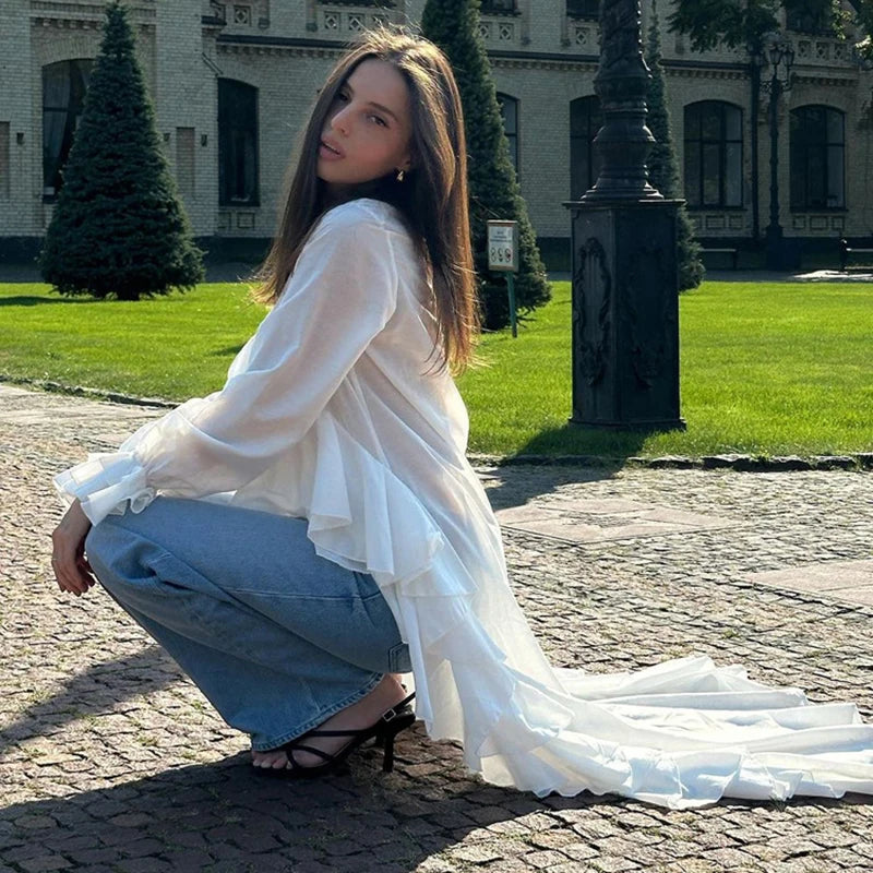 Woman in a white blouse and blue jeans squatting on a cobblestone path in front of a building.