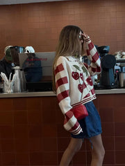 Person wearing a red and white sweater with cherry design in a coffee shop.