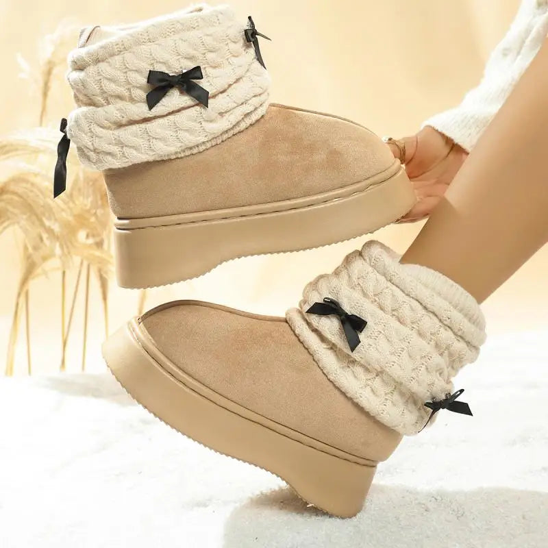 Beige winter boots with white cuffs and black bows worn by a person.