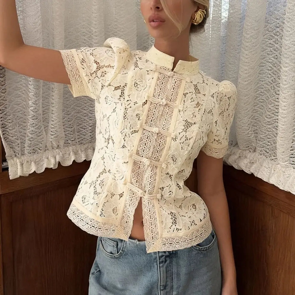 Woman wearing a white lace blouse with short sleeves and blue jeans in front of a curtain.