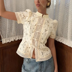 Woman wearing a white lace blouse with short sleeves and blue jeans in front of a curtain.
