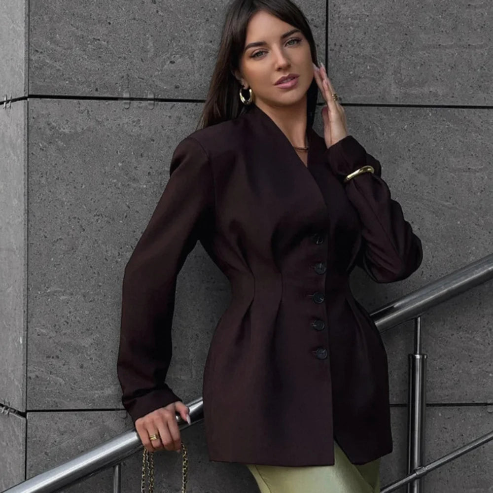 Woman wearing a dark brown blazer against a gray wall.