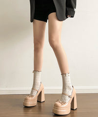 Person wearing beige platform shoes and patterned socks on a plain background