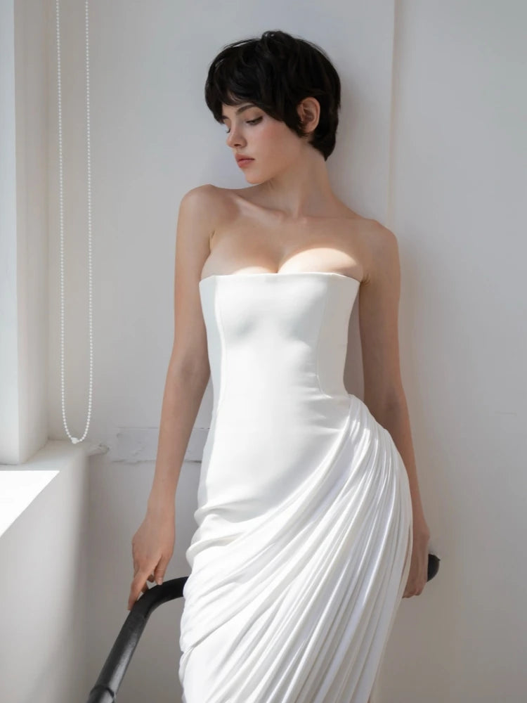Woman wearing a strapless white dress against a white wall