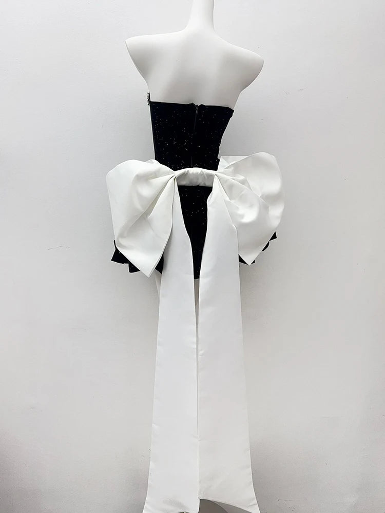 Mannequin wearing a black dress with a large white bow on a plain background