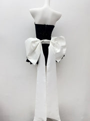 Mannequin wearing a black dress with a large white bow on a plain background