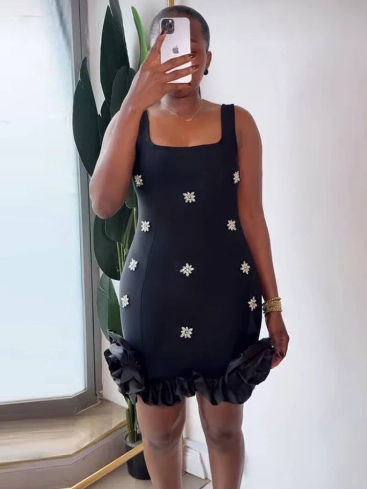 Person wearing a black dress with white floral patterns in a room with a plant.