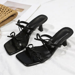 Black high-heeled sandals with bow details on a white background