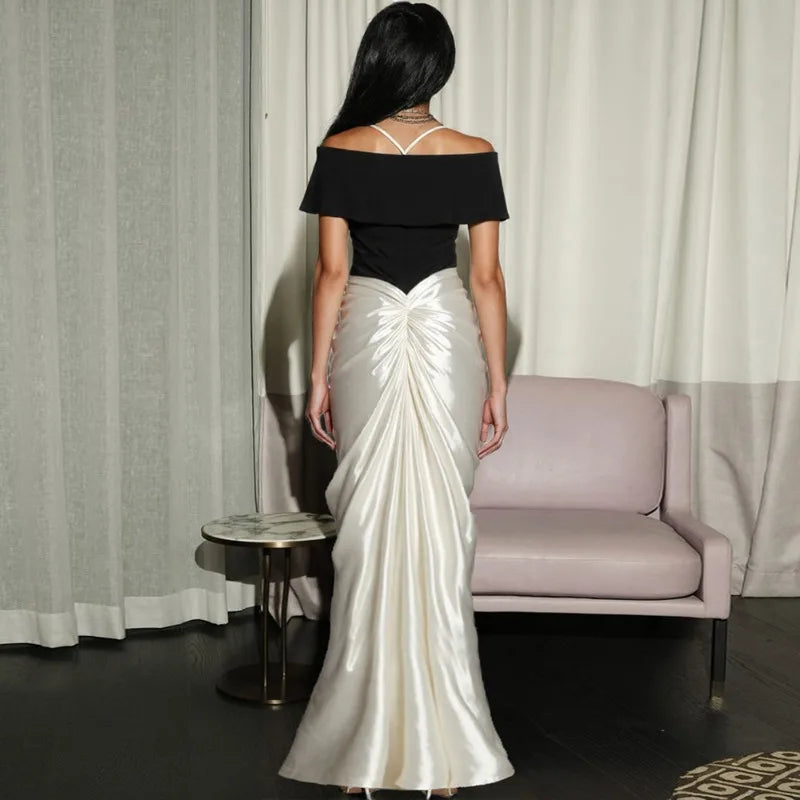 Woman wearing a black top and white satin gown in a room with curtains and a couch.