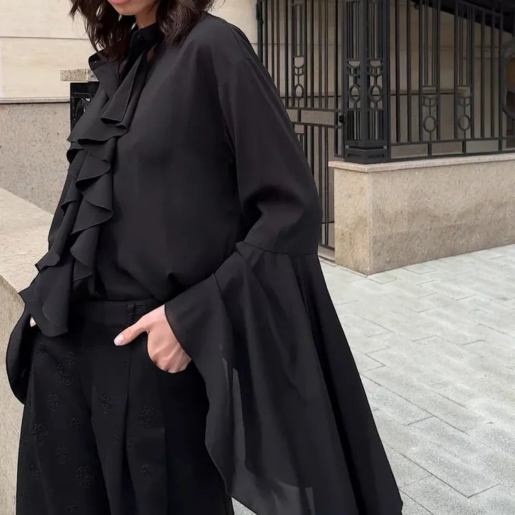Person wearing a black ruffled outfit standing on a street.
