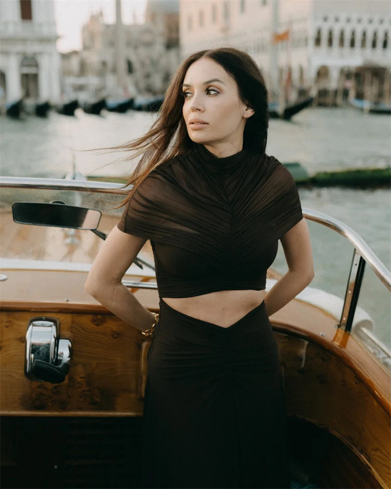 Woman in a black outfit standing on a boat with a cityscape in the background