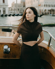 Woman in a black outfit standing on a boat with a cityscape in the background