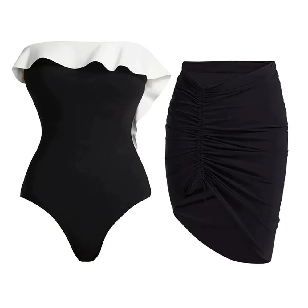 Flat lay of a black and white ruffle monokini next to a ruched black skirt.
