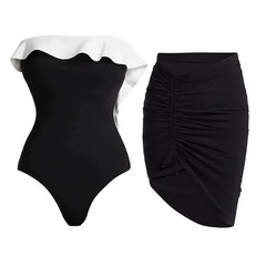 Flat lay of a black and white ruffle monokini next to a ruched black skirt.