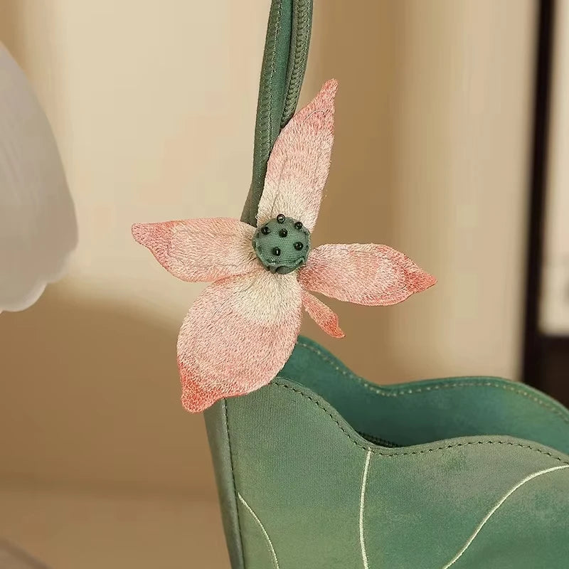 Green handbag with a pink embroidered flower detail on a beige background