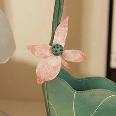Green handbag with a pink embroidered flower detail on a beige background
