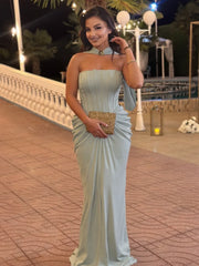 Woman in a light blue strapless dress holding a gold clutch on a paved walkway at night.