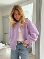 Woman wearing a purple cardigan and blue jeans indoors.
