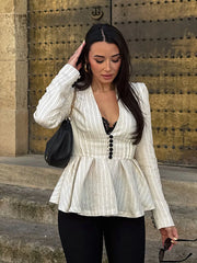 Woman in a white pinstripe peplum top standing in front of a large metal door.
