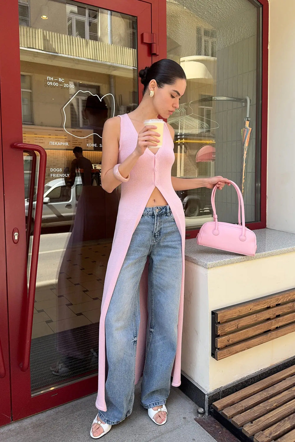 Woman in a pink dress and blue jeans holding a pink handbag outside a store.