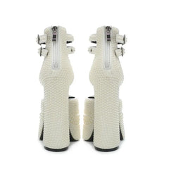 Pair of white high-heeled shoes with decorative elements on a white background
