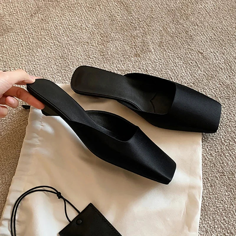 Black high-heeled shoes on a beige carpet with a white bag underneath.